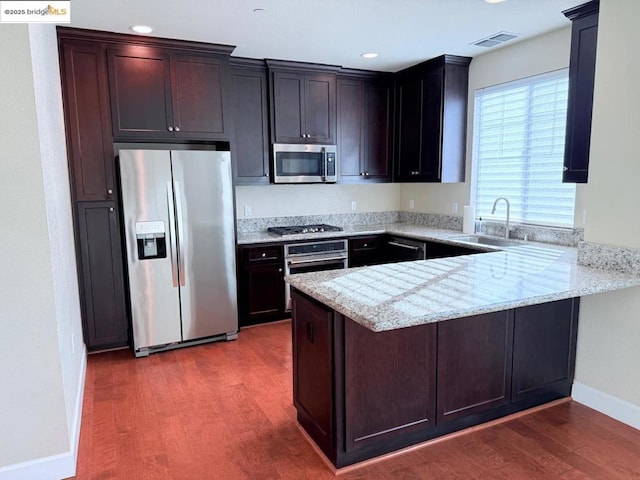 kitchen with kitchen peninsula, light stone countertops, dark hardwood / wood-style flooring, stainless steel appliances, and sink