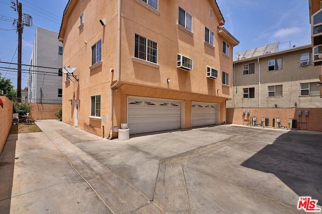 view of building exterior featuring a garage, a wall mounted AC, and central AC