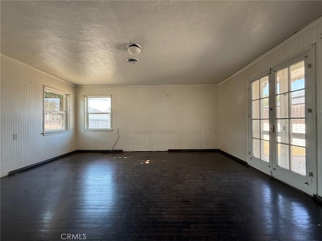 empty room with plenty of natural light, dark hardwood / wood-style floors, crown molding, and french doors