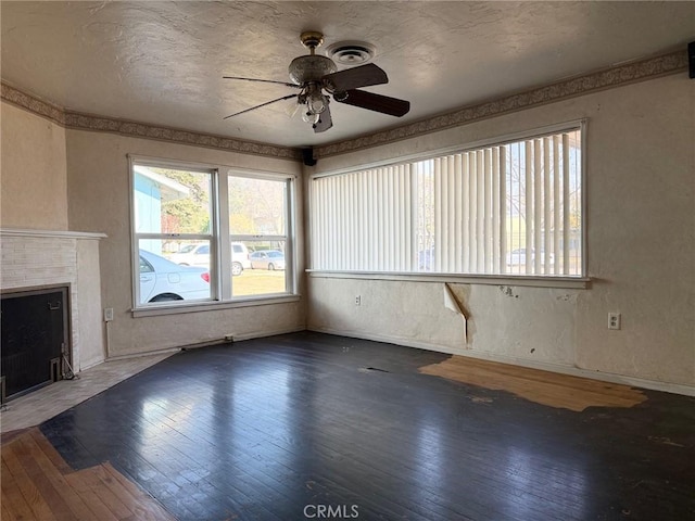 unfurnished living room with a textured ceiling, ceiling fan, dark hardwood / wood-style floors, and a tile fireplace