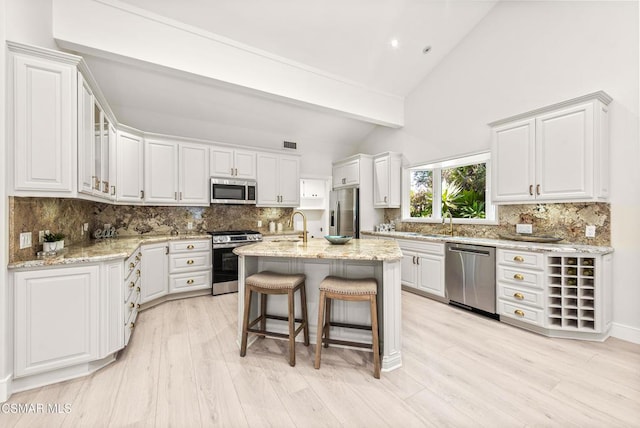 kitchen featuring stainless steel appliances, white cabinetry, a kitchen island with sink, and light stone counters