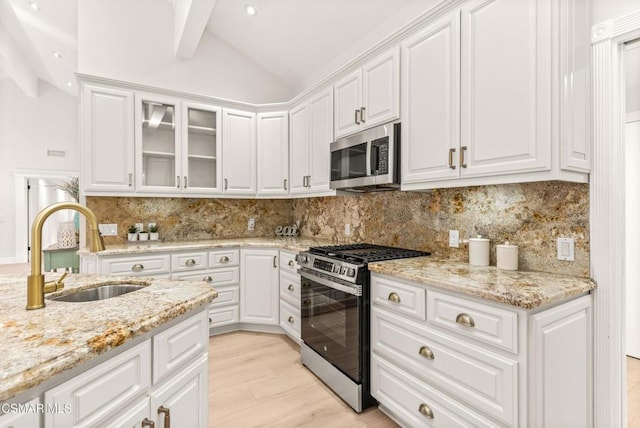 kitchen with white cabinetry, stainless steel appliances, sink, and vaulted ceiling with beams