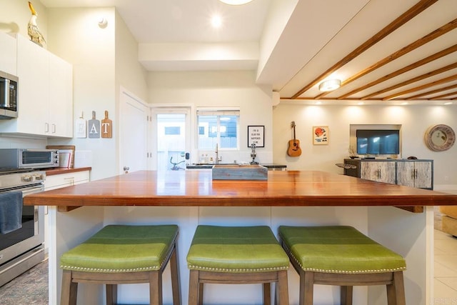 kitchen featuring stainless steel appliances, a kitchen breakfast bar, wooden counters, and white cabinets