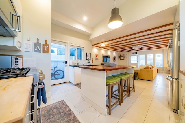 kitchen with butcher block counters, a breakfast bar area, white cabinetry, decorative light fixtures, and appliances with stainless steel finishes