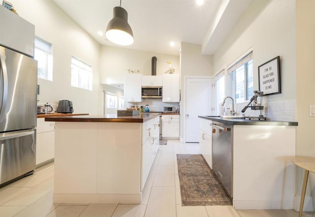 kitchen with pendant lighting, sink, appliances with stainless steel finishes, white cabinets, and a kitchen island