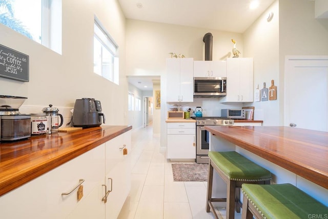 kitchen with butcher block countertops, appliances with stainless steel finishes, a high ceiling, white cabinets, and light tile patterned flooring