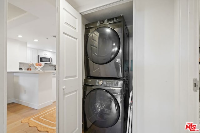 laundry area with light hardwood / wood-style flooring and stacked washer and clothes dryer