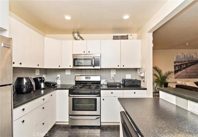 kitchen with decorative backsplash, white cabinetry, stainless steel appliances, and dark tile patterned flooring