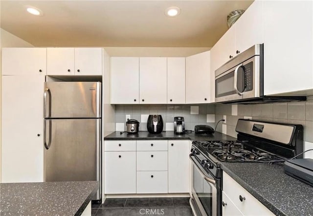 kitchen featuring appliances with stainless steel finishes, backsplash, dark tile patterned flooring, dark stone countertops, and white cabinets