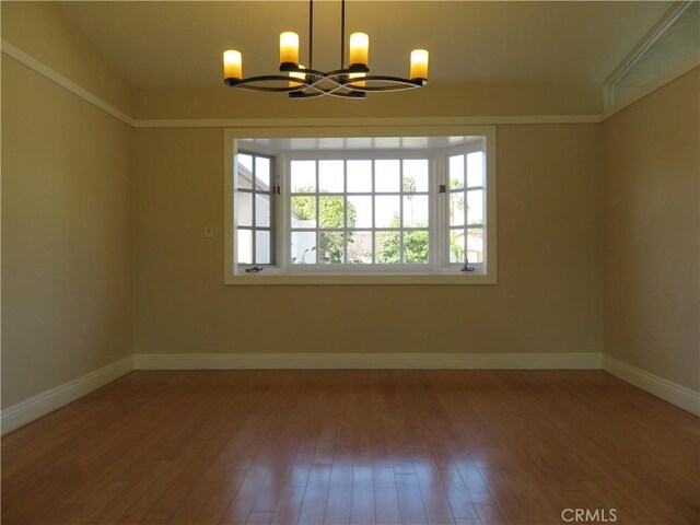 empty room featuring wood-type flooring and a notable chandelier