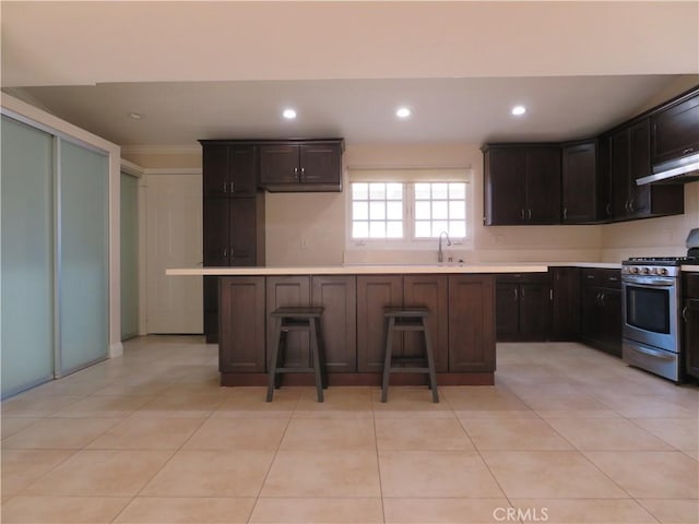 kitchen with stainless steel range with gas stovetop, light tile patterned floors, a center island, a breakfast bar area, and range hood