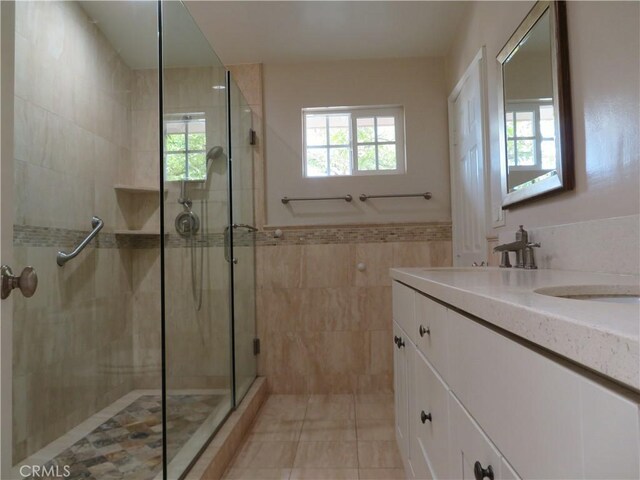 bathroom with tile patterned flooring, vanity, an enclosed shower, and tile walls