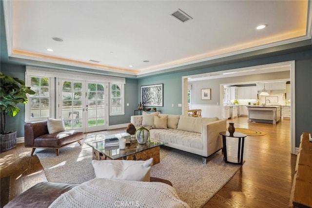 living area featuring wood finished floors, visible vents, baseboards, french doors, and a tray ceiling