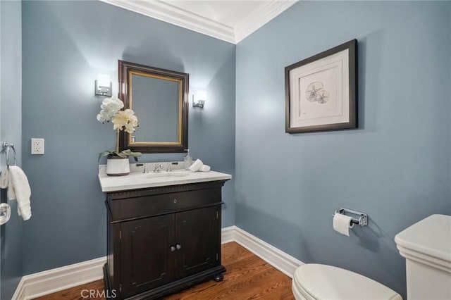 half bath with toilet, wood finished floors, vanity, baseboards, and ornamental molding