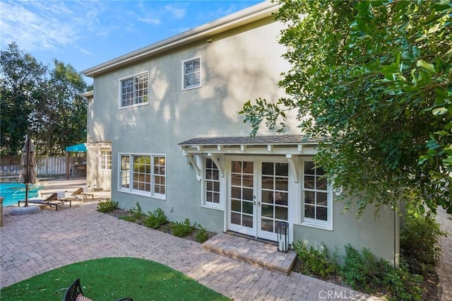 back of house featuring an outdoor structure, fence, french doors, stucco siding, and a patio area