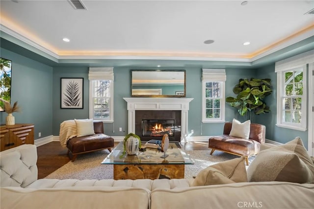 sitting room with a wealth of natural light, light wood-type flooring, a glass covered fireplace, and visible vents