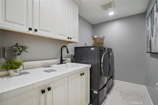 washroom featuring cabinet space, baseboards, washer and clothes dryer, a sink, and recessed lighting