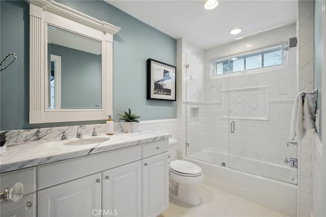 full bath featuring a wainscoted wall, toilet, combined bath / shower with glass door, vanity, and tile patterned flooring