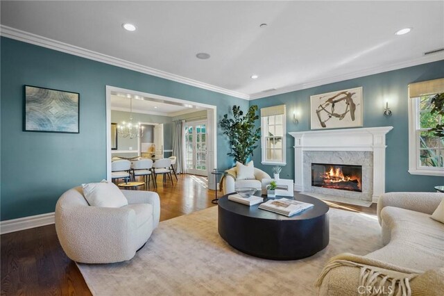 living room featuring crown molding, an inviting chandelier, a premium fireplace, and hardwood / wood-style flooring