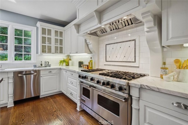 kitchen featuring dark wood-style flooring, custom range hood, appliances with stainless steel finishes, glass insert cabinets, and white cabinetry