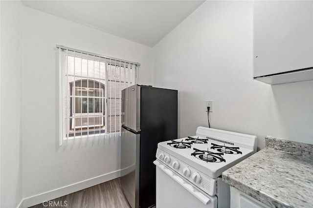 kitchen with white range with gas stovetop, stainless steel fridge, and hardwood / wood-style flooring