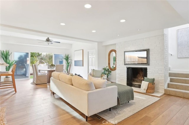 living room featuring a fireplace, light wood-type flooring, and ceiling fan