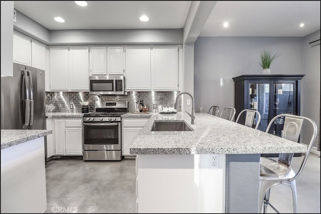 kitchen featuring sink, white cabinetry, a kitchen breakfast bar, stainless steel appliances, and concrete flooring