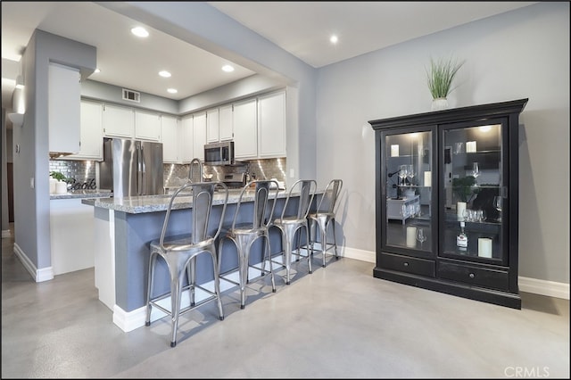 kitchen featuring appliances with stainless steel finishes, decorative backsplash, white cabinets, and light stone countertops