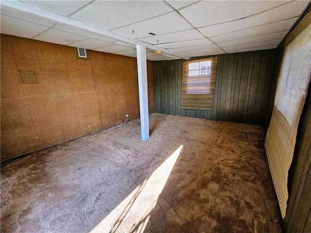 basement featuring a paneled ceiling, wooden walls, and carpet