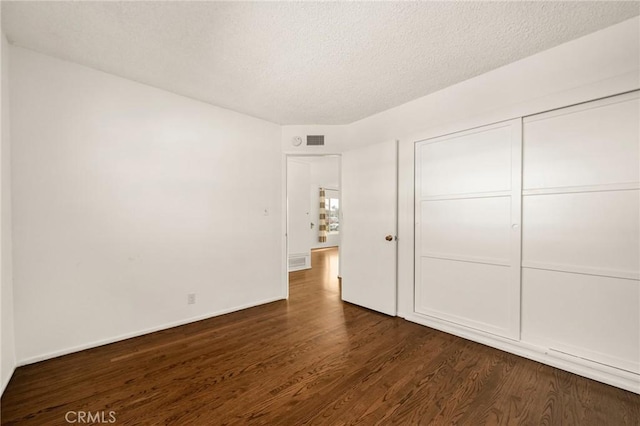 unfurnished bedroom featuring a textured ceiling, dark wood-type flooring, and a closet