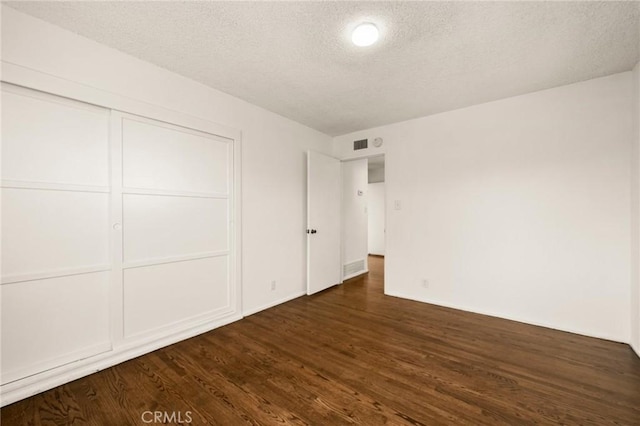 unfurnished bedroom featuring a textured ceiling, dark hardwood / wood-style floors, and a closet