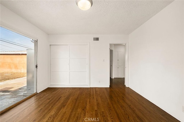 unfurnished bedroom with a textured ceiling, dark hardwood / wood-style flooring, and a closet