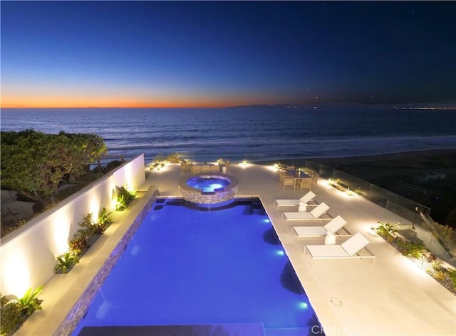 pool at dusk with an in ground hot tub, pool water feature, and a water view