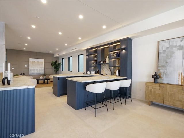 kitchen with a center island, light stone counters, a kitchen bar, and kitchen peninsula