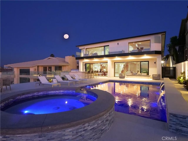 pool at twilight featuring an in ground hot tub, pool water feature, an outdoor bar, and a patio area