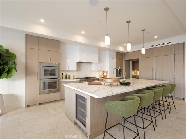 kitchen featuring a spacious island, sink, hanging light fixtures, beverage cooler, and light stone countertops