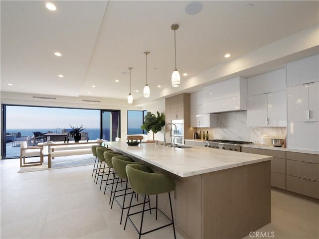 kitchen with pendant lighting, sink, white cabinets, a large island with sink, and a water view