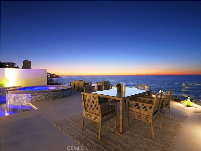 patio terrace at dusk with a swimming pool with hot tub and a water view