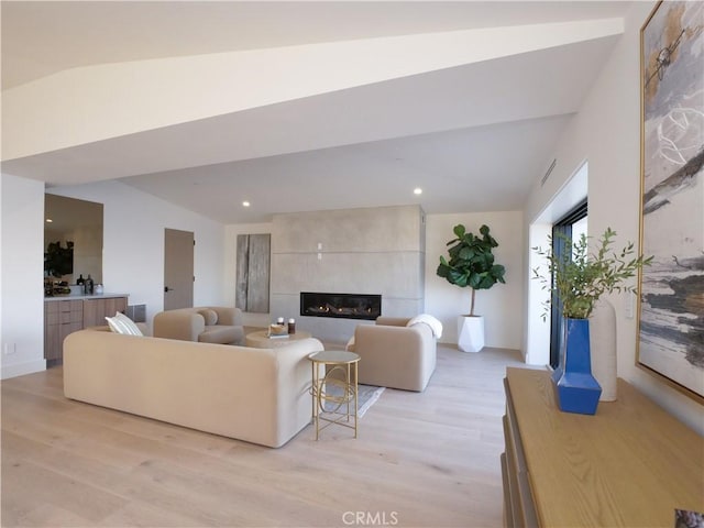 living room featuring a tiled fireplace, vaulted ceiling, and light hardwood / wood-style floors