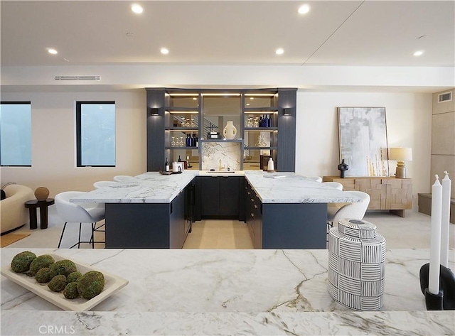 kitchen with a kitchen bar, sink, light stone counters, and kitchen peninsula