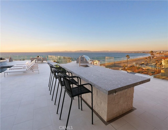 patio terrace at dusk with a water view, exterior kitchen, and an outdoor wet bar