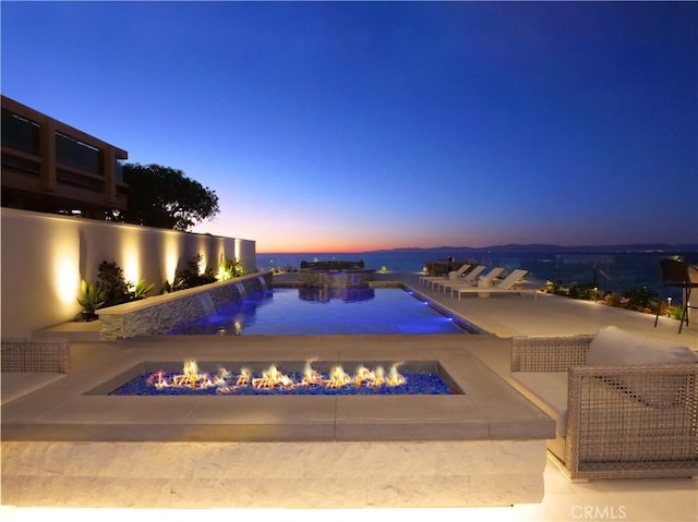 pool at dusk with a patio area and a fire pit