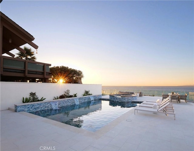 pool at dusk featuring a patio area and an in ground hot tub