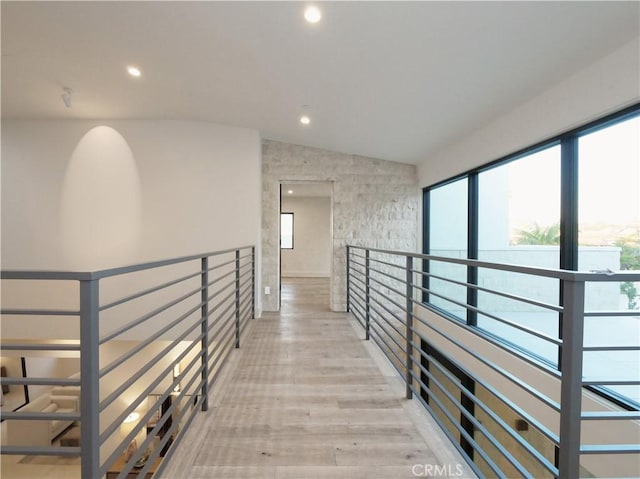 corridor featuring lofted ceiling, plenty of natural light, and light wood-type flooring