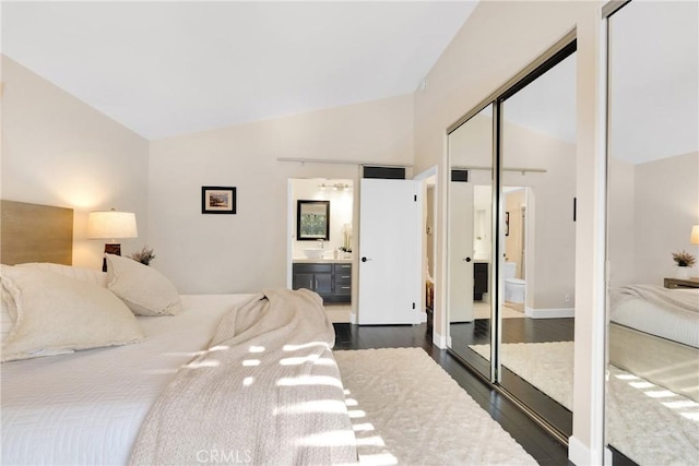 bedroom with a closet, dark hardwood / wood-style flooring, connected bathroom, and vaulted ceiling