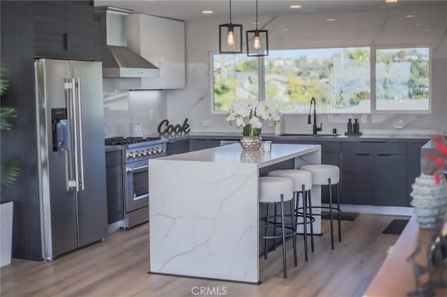 kitchen with sink, wall chimney exhaust hood, stainless steel appliances, decorative light fixtures, and a kitchen island