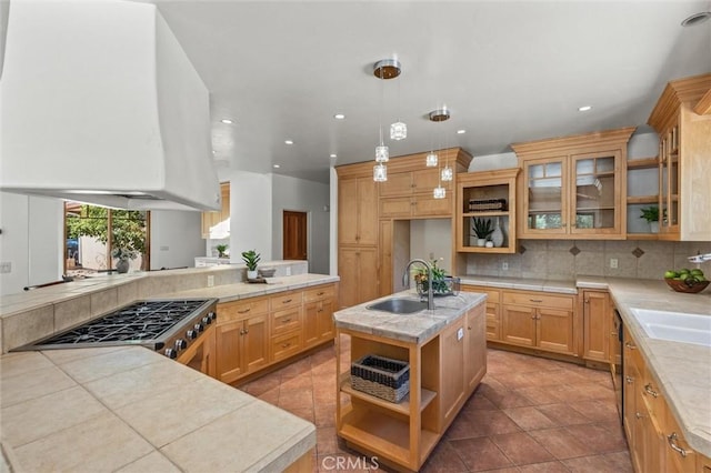 kitchen with a center island with sink, sink, hanging light fixtures, decorative backsplash, and range