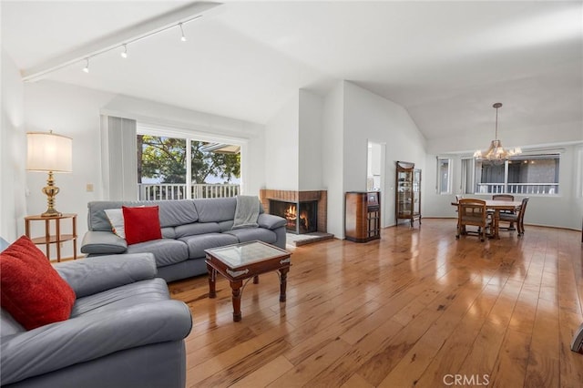 living room featuring rail lighting, a chandelier, vaulted ceiling, wood-type flooring, and a fireplace