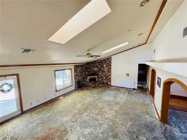 unfurnished living room with a wood stove, ceiling fan, lofted ceiling with skylight, and a textured ceiling