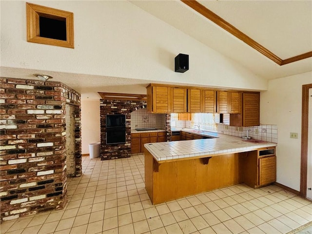 kitchen featuring tile countertops, decorative backsplash, kitchen peninsula, and high vaulted ceiling